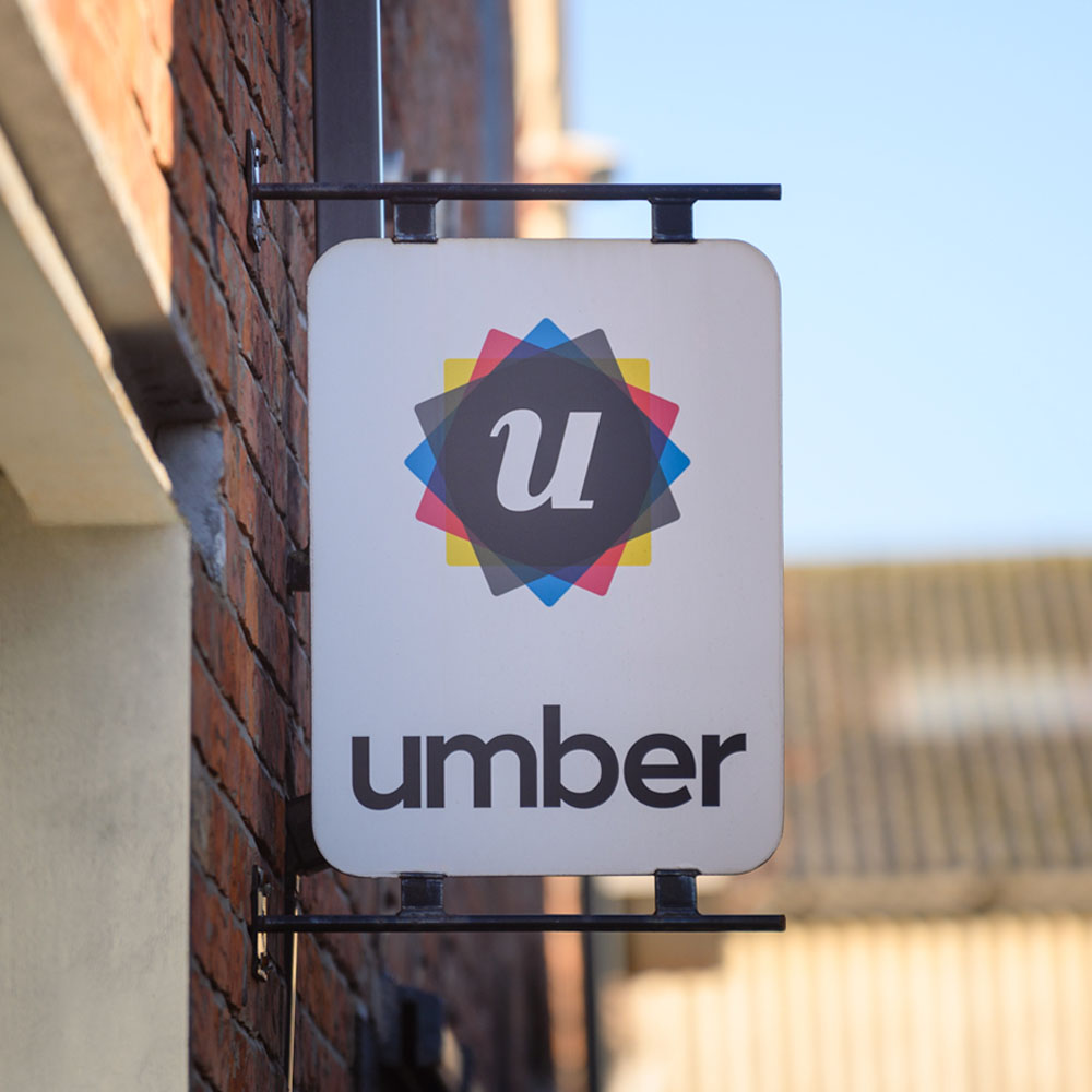 A wall-mounted sign displays a colourful geometric logo with the letter 'u' in the centre, above the word 'umber'. The scene is set against a clear blue sky.