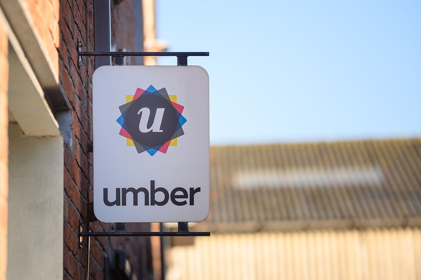 Brick wall sign for 'umber' featuring a stylised 'u' in a colourful geometric design. Bright, clear sky background, conveying a modern, upbeat tone.
