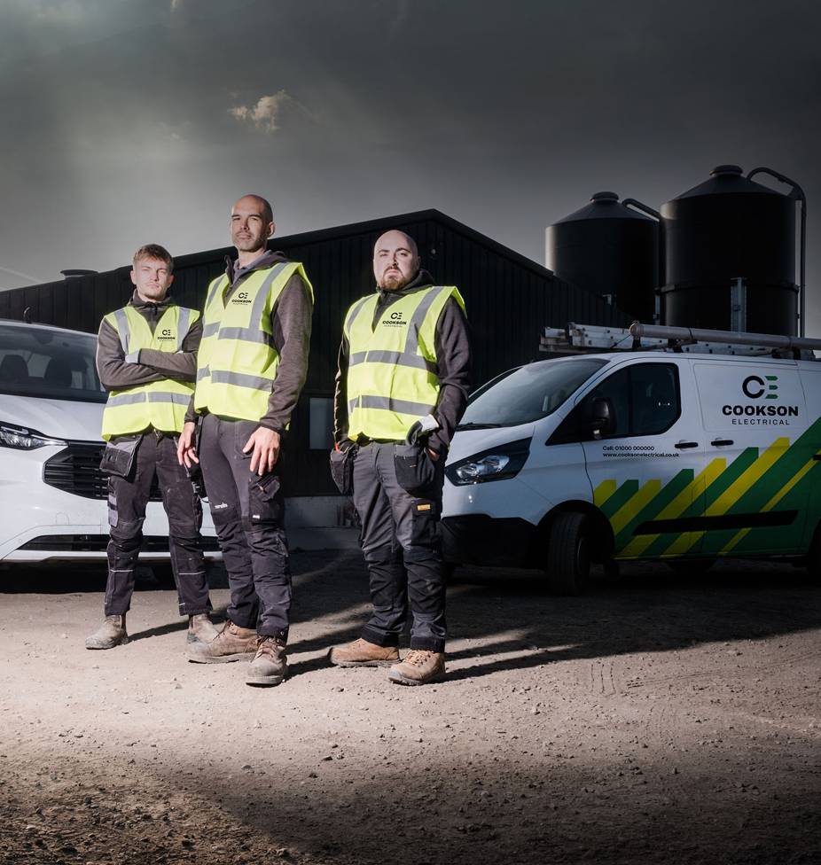 Three men stand confidently wearing high-visibility vests in front of vans with "Cookson Electrical" branding, under a cloudy sky, conveying professionalism.