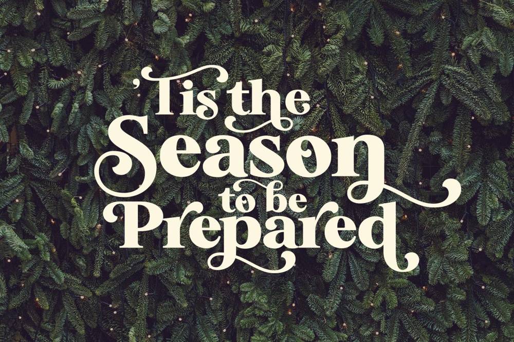 Elegant white text reading 'Tis the Season to be Prepared' overlays a lush evergreen background, evoking a festive and thoughtful atmosphere.