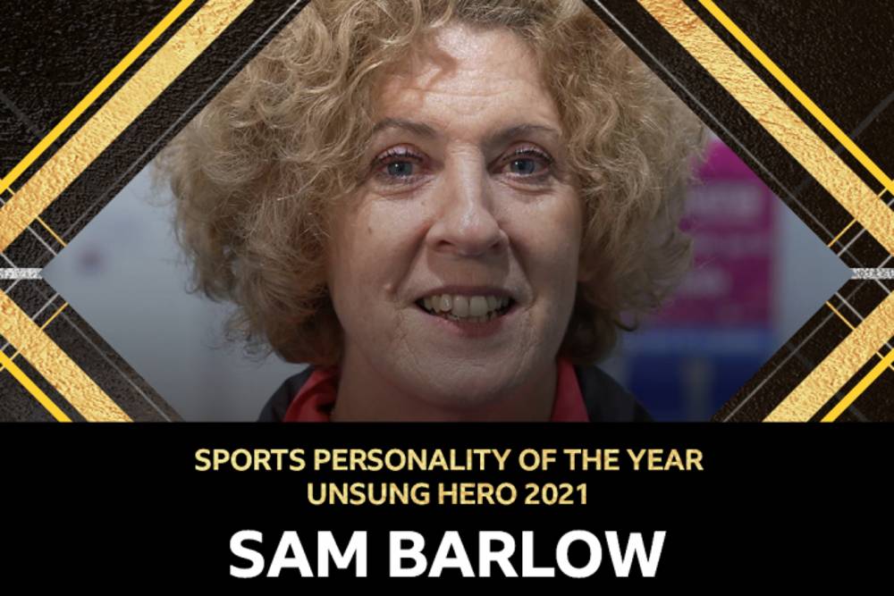 Close-up of a smiling person with curly hair, framed by a gold and black geometric border. Text reads: 'Sports Personality Unsung Hero 2021, Sam Barlow.'