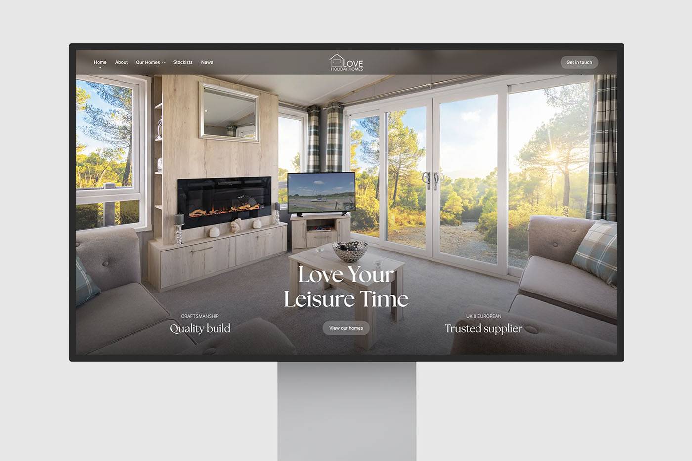 Modern website design displayed on a monitor, features a cozy living room with large windows, a fireplace, and inviting seating. Bright, peaceful ambiance.